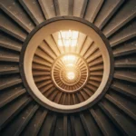 Escada em caracol vista de cima formando uma espiral que se fecha em direção ao centro iluminado